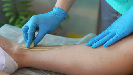 Close-up-in-the-beauty-salon-master-in-gloves-doing-the-procedure-to-remove-the-hair-on-the-legs-with-a-sugar-mixture