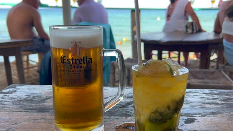 Nice-cold-beer-and-mojito-cocktail-at-a-beautiful-beach-bar,-refreshing-drinks,-enjoying-summer-with-dreamy-holiday-sea-view-in-Ibiza-Spain,-vacation-destination,-4K-shot
