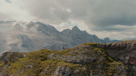 Parallax-aerial-shot-of-a-explorer-walking-on-top-of-a-mountain-ridge,-revealing-a-glacier-on-the-top-of-the-steep-mountains-in-the-background,-cinematic-grade