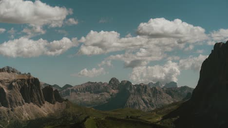 Timelapse-with-distant-steep-tall-mountains-in-the-background-green-valley-between-mountains,-partly-cloudy-sunny-day,-blue-sky,-cinematic-grade