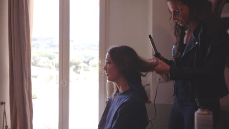 Girl-Sitting-Inside-the-Room-Having-Her-Hair-Done-by-a-Hairdresser-Using-A-Curling-Iron