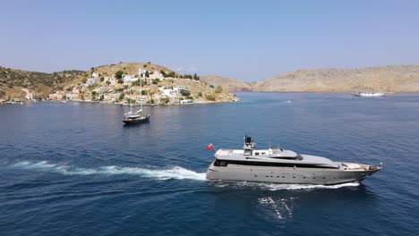 Luxurious-grey-yacht-leaving-harbor-Symi-in-Greece,-beautiful-summer-day,-aerial