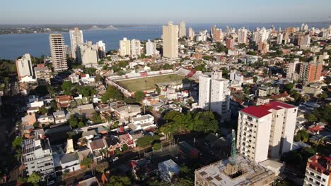 Aerial-view-of-the-coastal-city-of-Posadas-Misiones-Argentina,-drone-shot-of-densely-populated-coastal-city-cloudy-sky-with-soccer-stadium
