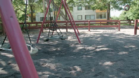 Empty-swings-swaying-at-the-playground-with-apartment-building-in-the-background