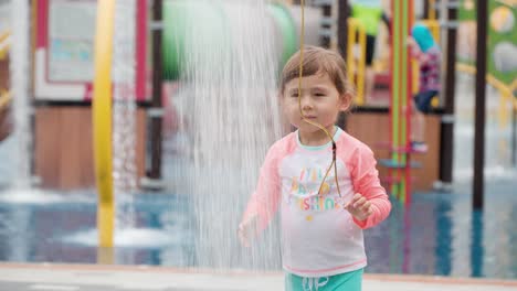 Lächelndes,-Glückliches-Kleines-Kind,-Das-An-Einem-Heißen-Sommertag-Mit-Der-Dusche-Auf-Dem-Wasserspielplatz-Im-Freien-In-Korea-Spielt