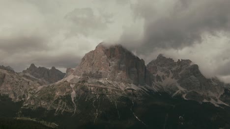 Aerial-view-with-distant-steep-tall-mountains-touching-the-clouds-green-forest-at-the-bottom,-Alps-rocky-mountains,-before-storm,-rainy-day,-cinematic-grade