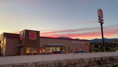 Beautiful-pink-orange-sunset-at-Burger-King-restaurant-in-Estepona-Spain,-amazing-sunset-at-Auto-King-drive-through,-4K-panning-left