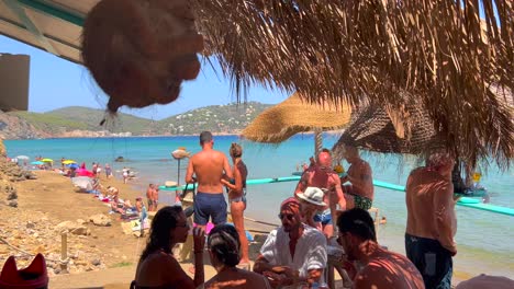 People-sitting-at-a-beautiful-beach-bar-and-enjoying-summer-drinks,-dreamy-holiday-destination-with-sea-view-in-Ibiza-Spain,-friends-family-hangout,-4K-shot