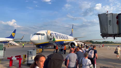 People-slowly-waiting-in-line-and-boarding-a-big-Ryanair-boeing-airplane-in-Bristol-international-airport-on-a-sunny-day,-holiday-vacation-time,-4K-shot
