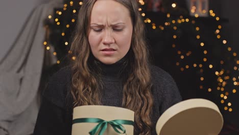 Curious-woman-opening-present-for-Christmas,-looking-unhappy-and-upset