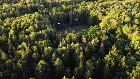 Drone-shot-tilting-toward-the-a-Soccer-Field-in-middle-of-dense,-sunlit-forest