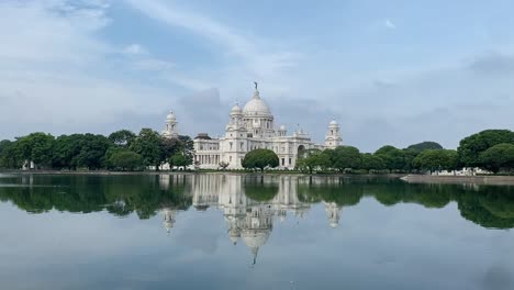 Shot-of-reflection-of-Victoria-Memorial-on-lake-water-surrounded-by-green-vegetation-in-Kolkata,-West-Bengal,-India-on-a-sunny-day
