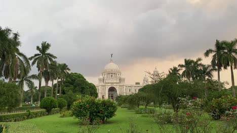 Shot-of-white-marble-monument--Victoria-Memorial-in-distance,-surrounded-by-green-vegetation-in-Kolkata,-West-Bengal,-India-on-a-cloudy-evening