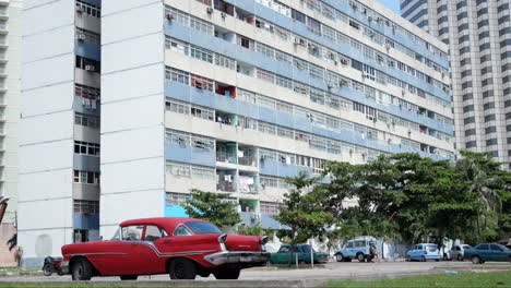 Vintage-Red-Car-Parked-Outside-Residential-Apartment-Building-In-Cuba