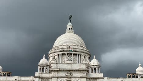 Low-angle-shot-of-Indian-flag-flying-on-top-of-Victoria-Memorial-which-is-a-large-marble-palace-in-Kolkata,-West-Bengal,-India-with-dark-clouds-in-the-background