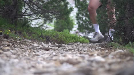 Feet-and-legs-of-a-hiker-hiking-along-a-rocky-path-with-green-vegetation-on-the-sides