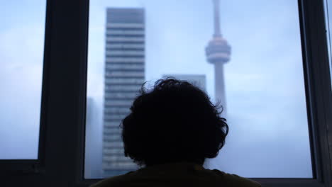 Ominous-Silhouetted-man-sitting-looking-out-to-the-Toronto-CN-Tower