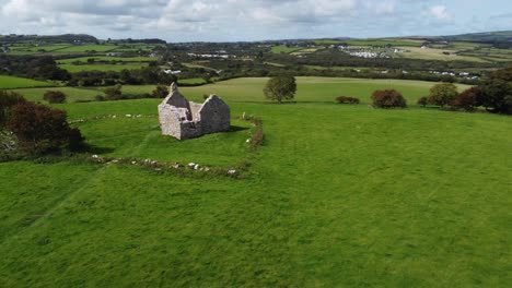 Establishing-aerial-view-circling-Capel-Lligwy-ruined-chapel-on-Anglesey-island-coastline,-North-Wales