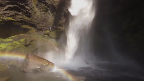 Nahaufnahme-Eines-Wunderschönen-Wasserfalls-In-Island-An-Einem-Sonnigen-Tag-Mit-Fliegenden-Vögeln-Und-Einem-Kleinen-Regenbogen-Vor-Den-Moosgrünen-Klippen-Und-Felsen