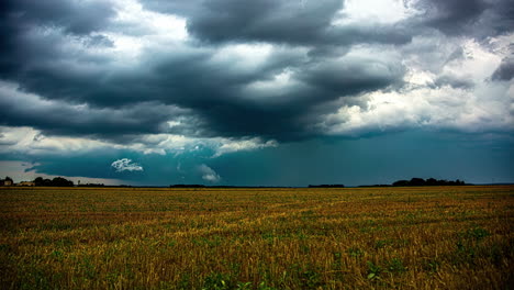 Powerful-dark-storm-clouds-flowing-above-rural-fields-with-working-farmers,-time-lapse-view