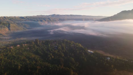 Aerial-tracking-shot-of-a-valley-covered-in-low-hanging-clouds,-sunrise-in-Bali,-Indonesia