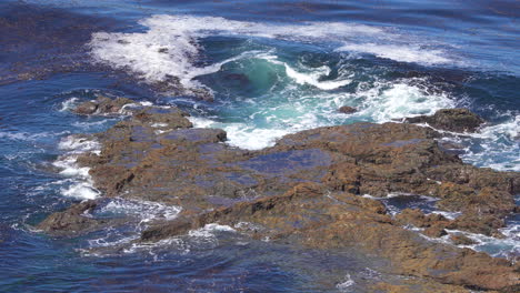 Ocean-waves-swirling-around-and-crashing-against-rocks-near-the-shoreline-of-Rancho-Palos-Verdes-in-slow-motion