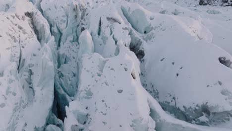 Aerial-view-over-irregular-ice-formations-in-Falljokull-glacier-covered-in-snow,-Iceland,-during-sunset