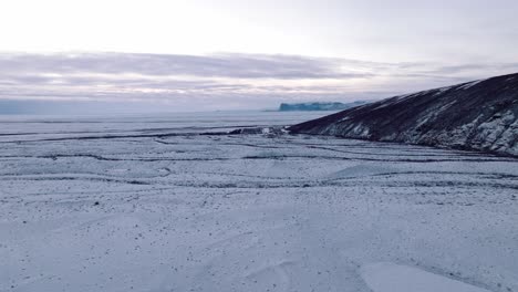 Aerial-landscape-view-over-Skaftafellsjokull-glacier-surrounding-mountains,-in-Iceland,-covered-in-snow,-at-dusk