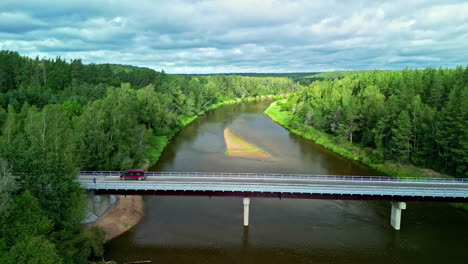 Newly-constructed-bridge-over-a-river-and-forested-countryside---pullback-aerial-reveal