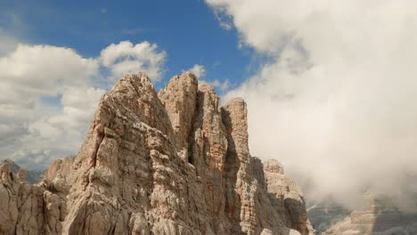 Drone-rises-up-Lagazuoi-mountain-in-the-Italian-Dolomites,-breaking-through-the-cloud-shroud-covering-the-rugged-ridge