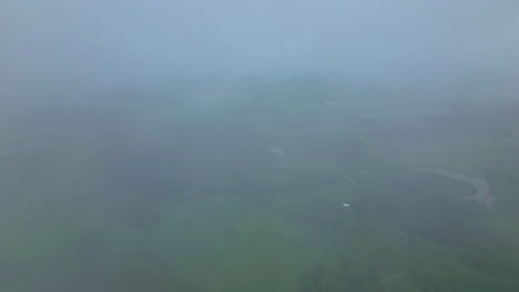 Looking-through-the-fog-or-clouds-at-green-countryside-farmlands---aerial