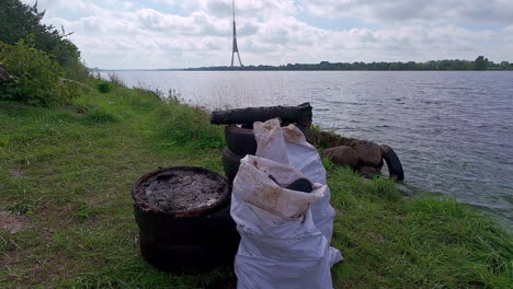 Ausrangierte-Gummireifen-Und-Weißer-Müllsack-An-Einem-Flussufer-Mit-Blick-Auf-Den-Fluss-Daugava-In-Riga,-Lettland
