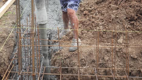 Builder-pours-concrete-from-pump-hose-into-house-foundation-rebar-trench