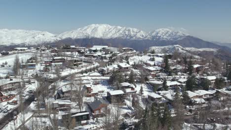 Aerial-view-of-ski-resort-town-with-snow-capped-mountains-in-Background,-Parallax-motion-shot