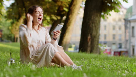 Young-woman-use-mobile-smartphone-celebrating-win-good-message-news-outdoors-in-urban-city-park