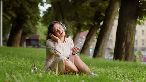 Mujer-Joven-Feliz-Con-Auriculares-Inalámbricos-Eligiendo,-Escuchando-Música-En-Un-Teléfono-Inteligente-Bailando-Al-Aire-Libre