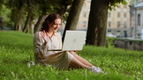 Woman-making-video-laptop-webcam-conference-call-with-friends-or-family-sitting-on-grass-in-park