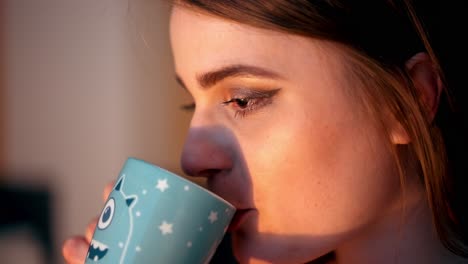 Close-up-of-a-girl-drinking-from-a-mug-at-home-with-the-sunrise-shining-through