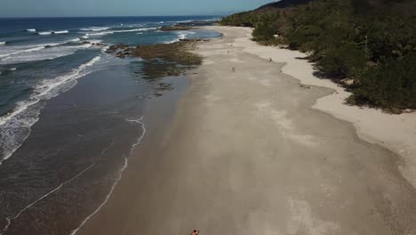 Drone-footage-over-a-tropical-beach,-people-walking-on-the-sand,-Santa-Teresa,-Costa-Rica