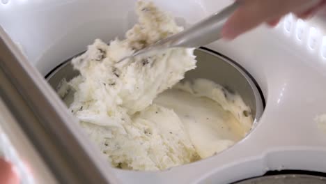 Hand-mixing-vanilla-chocolate-chip-ice-cream-in-display-freezer,-closeup