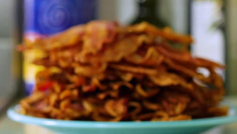 Pile-of-crispy-bacon-strips-stacked-on-plate-on-counter,-close-up-focus-pull