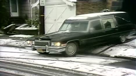 1980S-HEARSE-WITH-COFFIN-PULLING-OUT-ONTO-SNOW-COVERED-ROAD