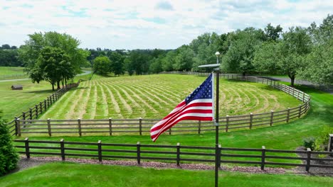 American-flag-waving-in-front-of-fenced-in-meadow-for-horses-in-USA