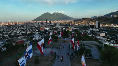 Aerial-view-over-flags-on-top-of-the-Bishopric-Hill,-sunset-in-Monterrey,-Mexico