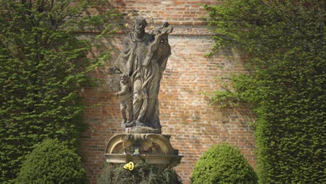 A-sandstone-statue-of-a-saint-with-a-cross-and-a-golden-halo-in-the-Brevnov-Monastery-garden-in-Prague