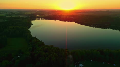 Golden-sunrise-or-sunset-over-lake-and-woodland-landscape,-aerial-view