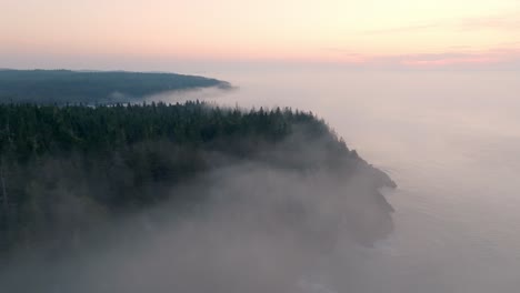 Wunderschöne-Drohnenaufnahme-Des-Sonnenaufgangs-über-Dem-Nebligen-Küstenwald-Von-Maine
