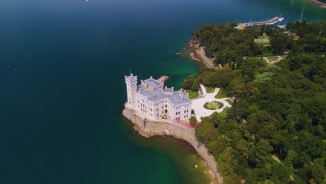 Through-the-lens-of-a-drone-camera,-one-can-behold-the-striking-beauty-of-the-Miramare-Castle,-proudly-positioned-against-the-seafront