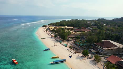 Parallax-of-Gili-Trawangan-Island-Soft-Sand-Public-Beach-Coast-with-Idyllic-Turquoise-Sea-and-Travel-Tour-Boats-Moored-in-Lombok-Indonesia,-establishing-aerial-shot