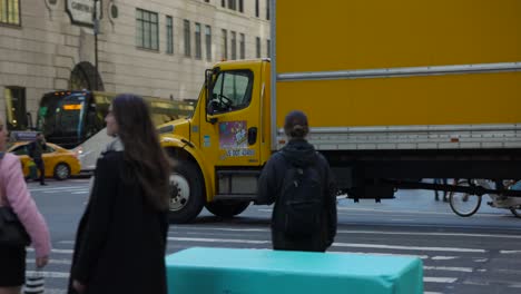 Slow-motion-tracking-shot-of-a-yellow-delivery-truck-crossing-busy-intersection-in-New-York-City,-USA